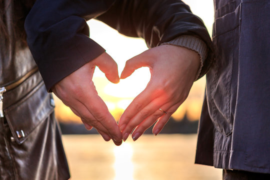Mann und Frau formen aus ihren Händen ein Herz beim Sonnenuntergang am See