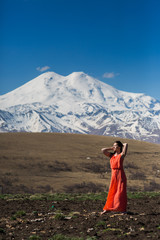 brunette slim girl in long red dress on the background of high snow-capped mountains 