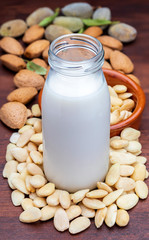 Almond milk in glass bottle. Includes peeled almonds. On rustic wooden background.