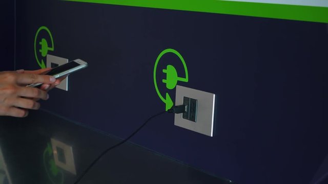 Close up of female hand plugging in mobile phone usb cable into electrical socket of charging station in airport