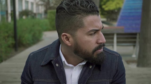 Nervous man looking away outdoor. Anxious bearded man sitting, touching face and looking aside on street. Emotion concept