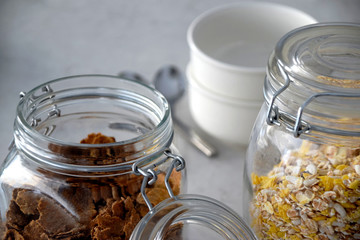 Close up on jars filled with breakfast cereals and with bowls and spoons in the background