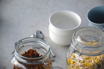 Jars filled with muesli and cornflakes. In the background are spoons and bowls