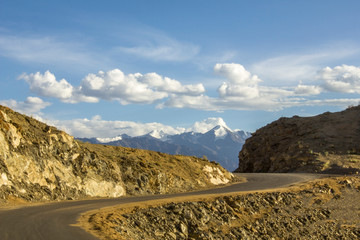 winding asphalt road in the desert mountains against the snowy peaks under a blue sky with white clouds