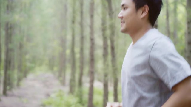 Healthy handsome young Asian Athlete man in sports clothing legs warming and stretching her arms to ready for running on forest trail. Lifestyle active men exercise in the forest concept.