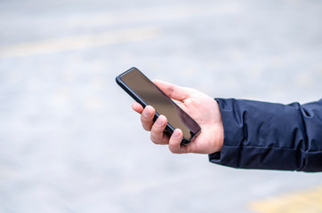 Closeup of man’s hand in jacket holding black smart phone