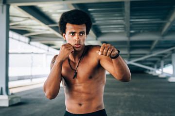Fototapeta na wymiar Bare-chested kickboxer standing under a bridge in combat stance