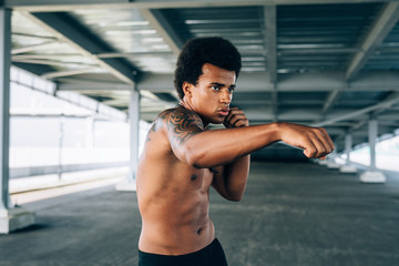 Fototapeta na wymiar Young bare chested kickboxer doing shadow boxing, practicing his punches outdoors