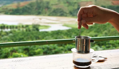 Tuinposter Brewing coffee luwak in the morning in nature. View of the coffee plantation. Man's hand with a spoon and coffee kettle © Olya Сhe