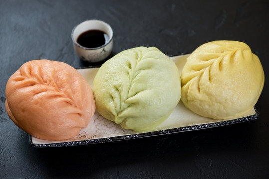 Korean steamed pjan-se or pigodi pies of different color served on a plate, studio shot on a black stone background
