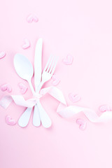 Fototapeta na wymiar Festive table setting for Valentines Day with fork, knife and hearts on pink pastel background.Set of silverware .Romantic dinner. Space for text. Top view