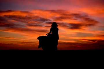 Silhouette of young woman with long dress at sunrise  on the beach 