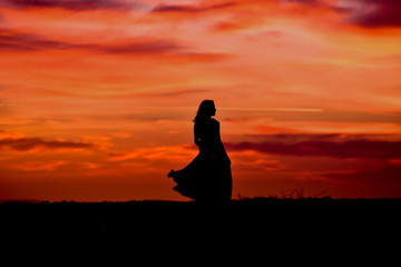 Silhouette of young woman with long dress at sunrise  on the beach 