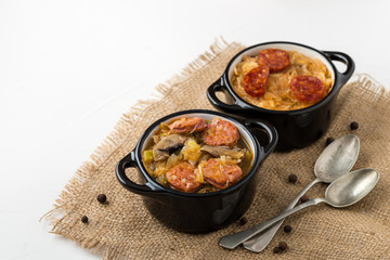 Slovak Christmas national cabbage soup in two small black pots with sausage on the jute background.