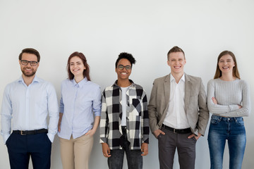 Diverse happy business people standing near wall looking at camera