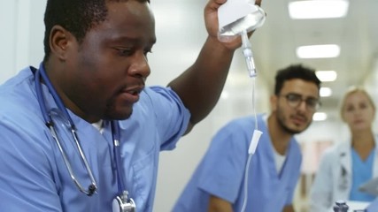 Dolly shot of emergency room male nurses administering oxygen and IV fluids to critical patient and rushing him to surgery. Female doctor in lab coat giving instructions and running behind them - Powered by Adobe
