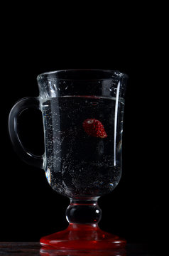 Strawberry in a glass of water with a black background.