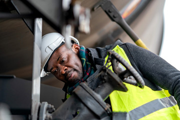 Afro-American train mechanic wearing safety equipment (helmet and jacket) checking and inspecting gear train