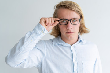 Serious young fair-haired man adjusting glasses