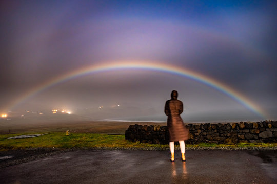 Lady observing very rare moonbow during the night above Staffin bay - Isle of Skye, Scotland