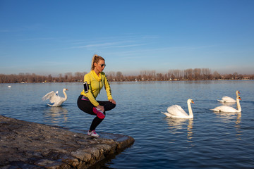 young woman jogging and workout by the river full of swans in city 