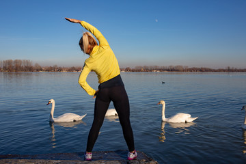 young woman jogging and workout by the river full of swans in city 