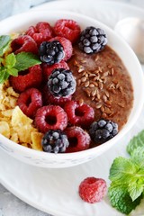Sunday Breakfast. Oatmeal porridge with banana and flax seed, raspberries, blackberries, corn flakes, honey and mint, selective focus. Useful food, diet. Plate or cup with vegan porridge, smoothies 