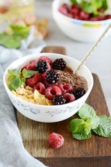 Sunday Breakfast. Oatmeal porridge with banana and flax seed, raspberries, blackberries, corn flakes, honey and mint, selective focus. Useful food, diet. Plate or cup with vegan porridge, smoothies 