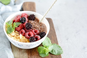 Sunday Breakfast. Oatmeal porridge with banana and flax seed, raspberries, blackberries, corn flakes, honey and mint, selective focus. Useful food, diet. Plate or cup with vegan porridge, smoothies 