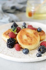  Sunday breakfast with cheesecake, honey, fresh berries  and mint. Cottage cheese pancakes or curd fritters decorated honey and berries in plate on blue table top view. Healthy and diet breakfast.