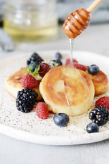  Sunday breakfast with cheesecake, honey, fresh berries  and mint. Cottage cheese pancakes or curd fritters decorated honey and berries in plate on blue table top view. Healthy and diet breakfast.