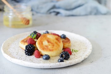  Sunday breakfast with cheesecake, honey, fresh berries  and mint. Cottage cheese pancakes or curd fritters decorated honey and berries in plate on blue table top view. Healthy and diet breakfast.