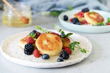  Sunday breakfast with cheesecake, honey, fresh berries  and mint. Cottage cheese pancakes or curd fritters decorated honey and berries in plate on blue table top view. Healthy and diet breakfast.