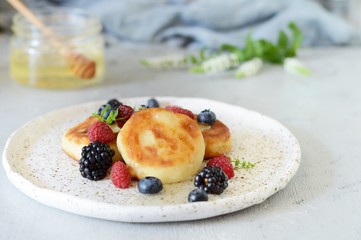  Sunday breakfast with cheesecake, honey, fresh berries  and mint. Cottage cheese pancakes or curd fritters decorated honey and berries in plate on blue table top view. Healthy and diet breakfast.