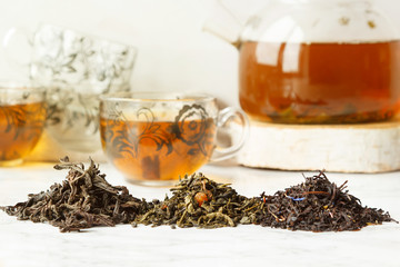 Black and green dry tea on the background of a teapot and cups with a drink. Different varieties of...