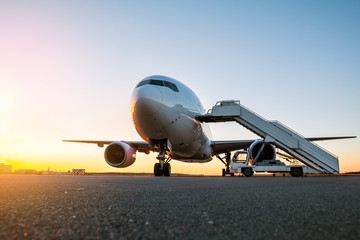 White wide body passenger aircraft with a boarding steps at the airport apron in the evening sun