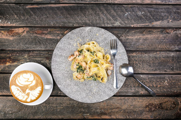 Fettuccine pasta with Seafood in old wooden table top view. Served with cutlery and a cup of coffee