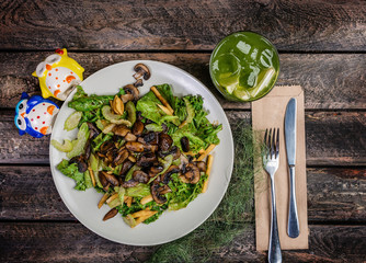Fresh vegetable salad with mushrooms, apples, lettuce, celery on the wooden table. Served by cutlery and fresh lemonade.