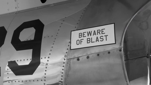 Tilt up to BEWARE of BLAST near engine of 1950s fighter jet. F-86 Sabre. Handheld shot with stabilized camera. Black and white.