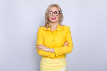 Beautiful blonde business woman wearring eyeglasses and yellow suit over white background in studio