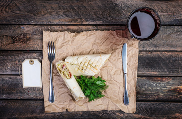 Tortilla wrap with chicken breast and vegetables. Served by cutlery and fresh lemonade on a wooden background.