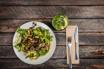 Fresh vegetable salad with mushrooms, apples, lettuce, celery on the wooden table. Served by cutlery and fresh lemonade.