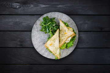 Sandwich with chicken and vegetables on a ceramic plate. On black wooden background, top view