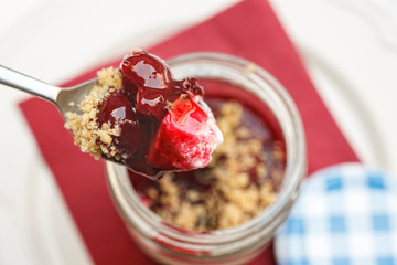 Spoonful of sour cherry cheese cake in a glass jar with biscuit crumbs