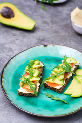 Appetizing bruschetta with salmon, butter, avocado and arugula on a plate