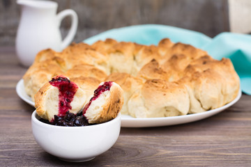Broken slice of monkey bread in black currant jam in a bowl on a wooden table
