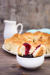 Broken slice of monkey bread in black currant jam in a bowl on a wooden table