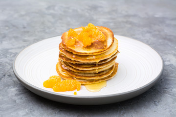 Delicious homemade pancakes with tangerines and honey on a plate on the table