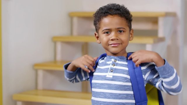 Medium shot of little African boy putting on school backpack and then looking at camera