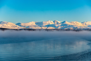 steam rising from the lake and snow-covered mountains, Lofoten Islands, Norway